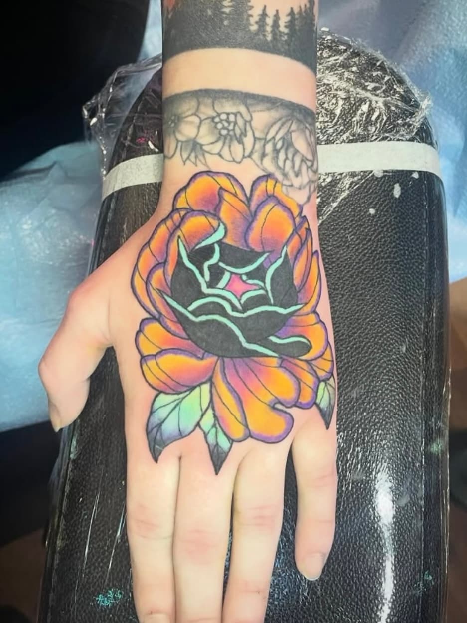 Vibrant orange and purple rose tattoo with black center on hand
