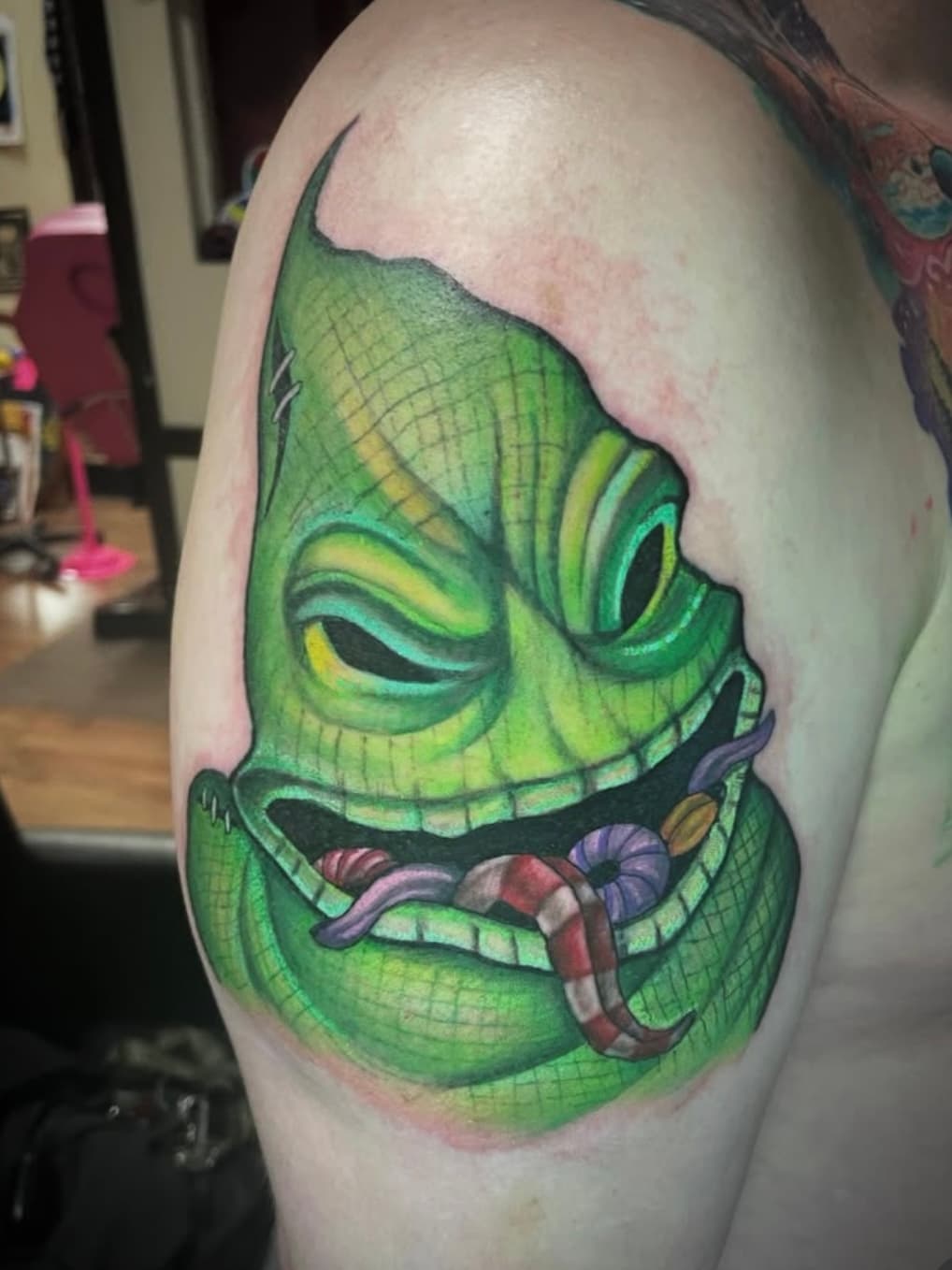 Green tiki mask tattoo with crossed tongue on person's upper arm