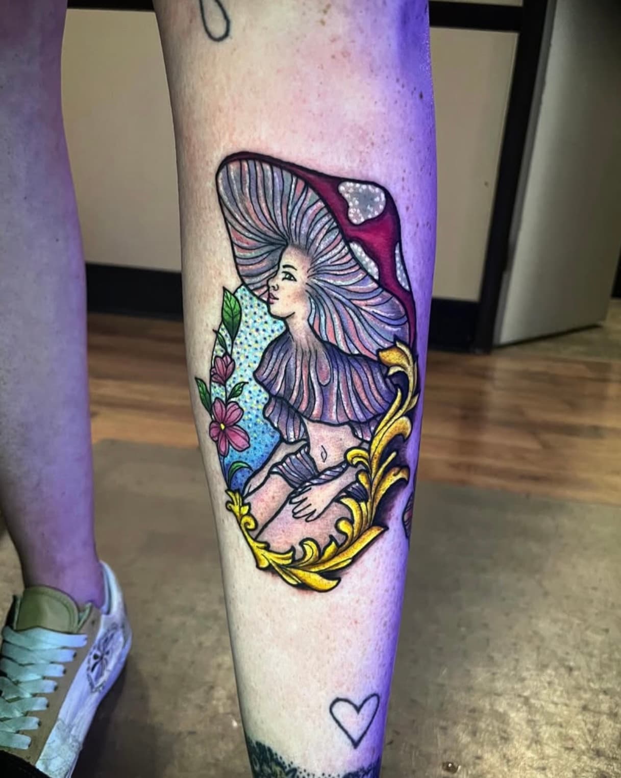 Colorful tattoo of fairy girl with flowing hair under mushroom cap with ornate gold frame