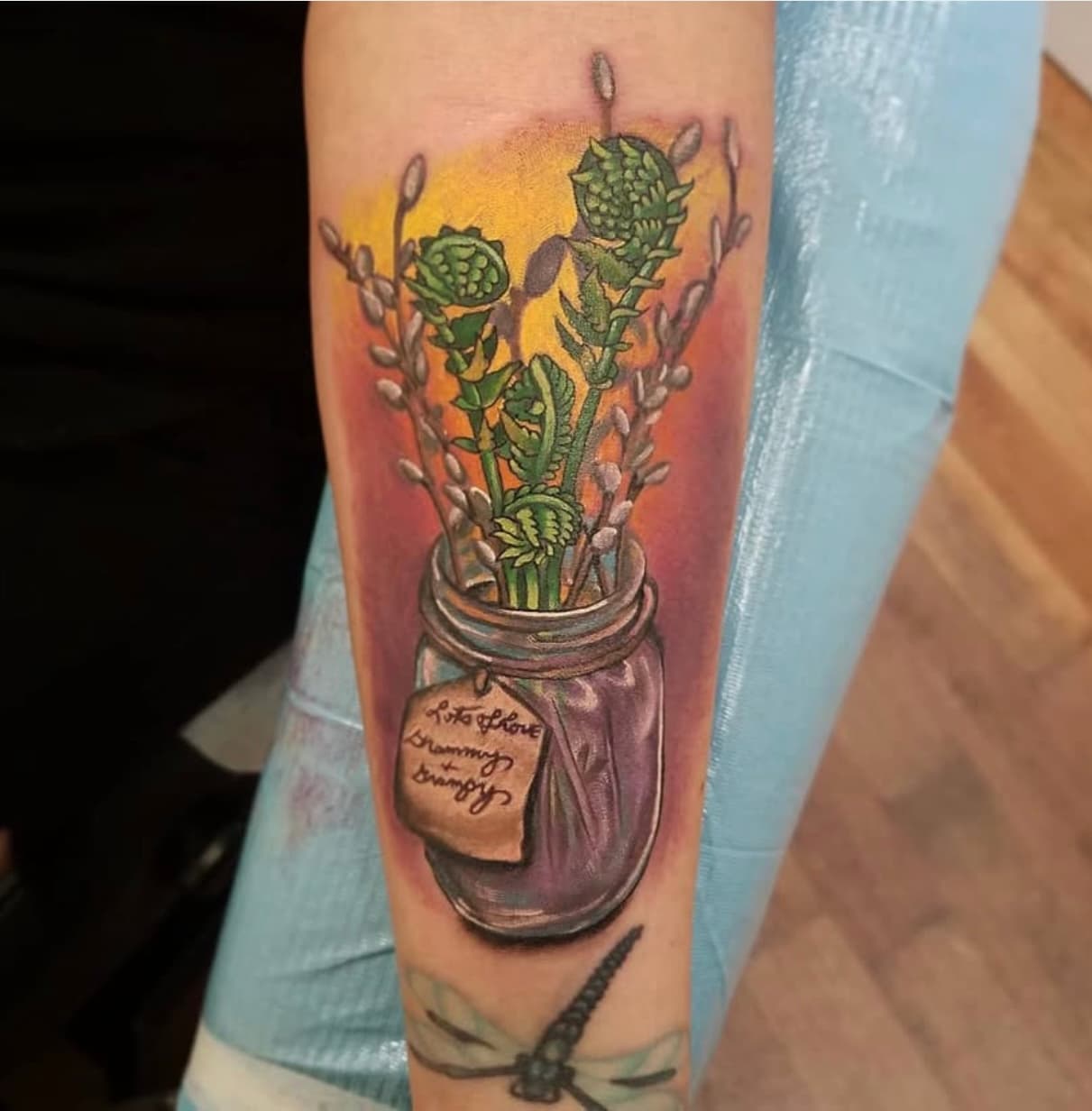 Forearm tattoo of ferns and pussy willows in mason jar with sunset backdrop