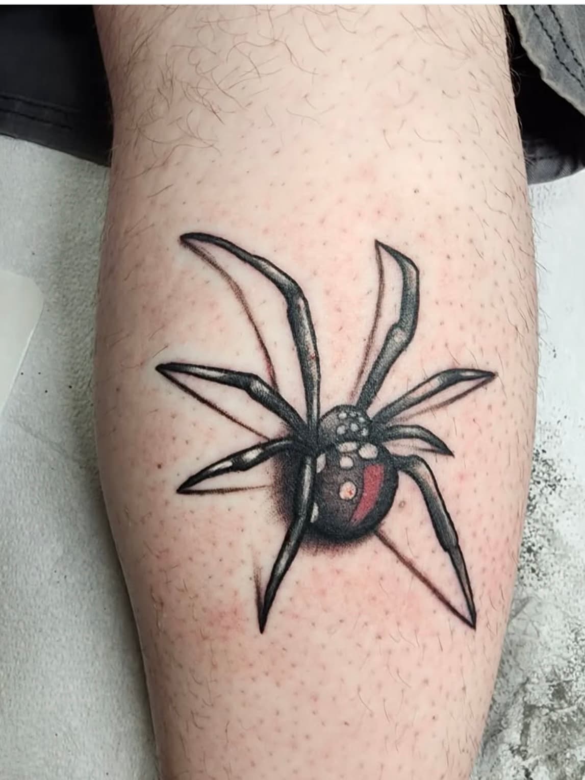Black widow spider tattoo with red hourglass marking on calf