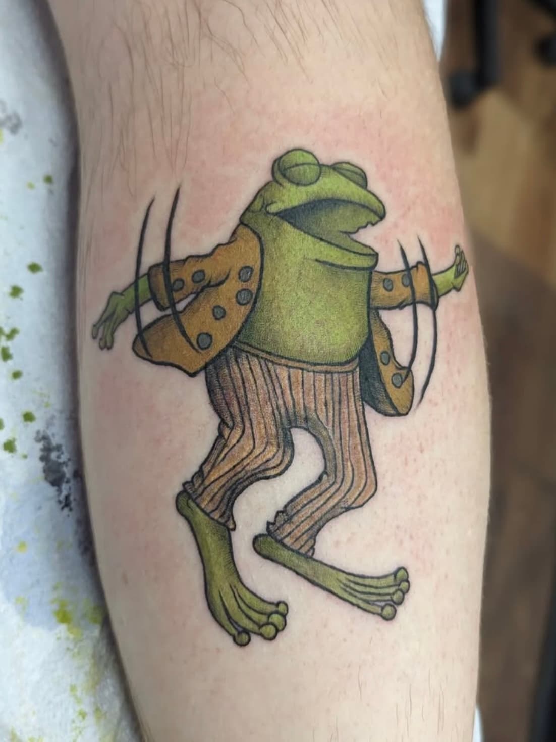 Colorful cartoon frog tattoo with spotted vest and striped pants on forearm