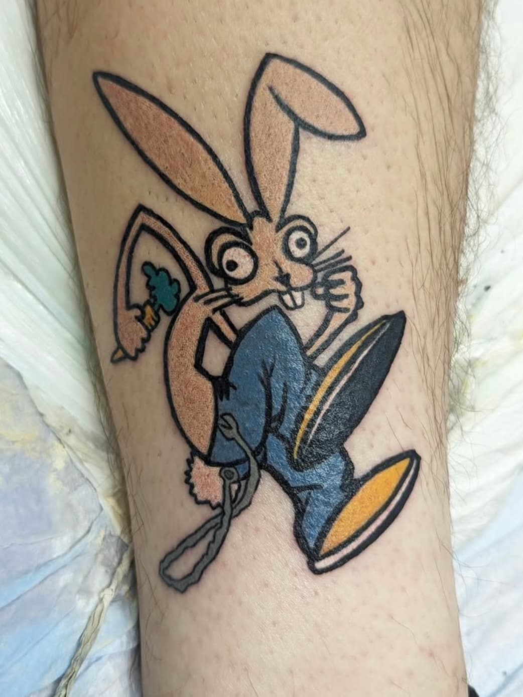 Cartoon rabbit tattoo in blue pants and shoes on client's leg