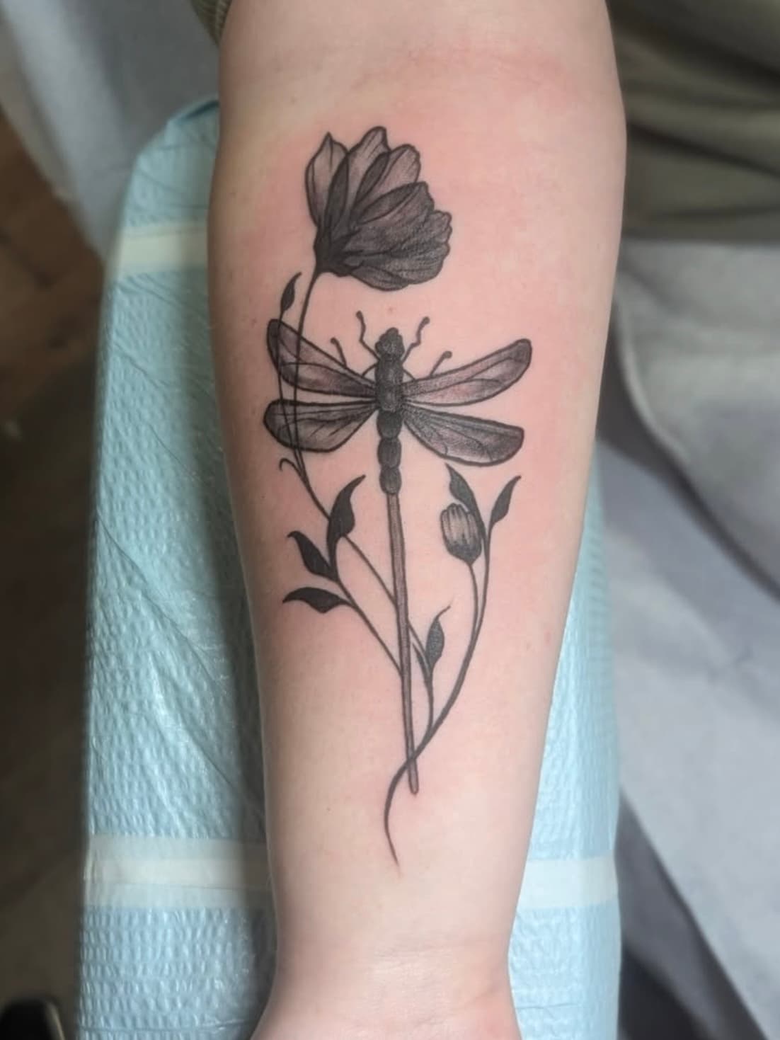 Black and gray tattoo of dragonfly with wildflowers on forearm