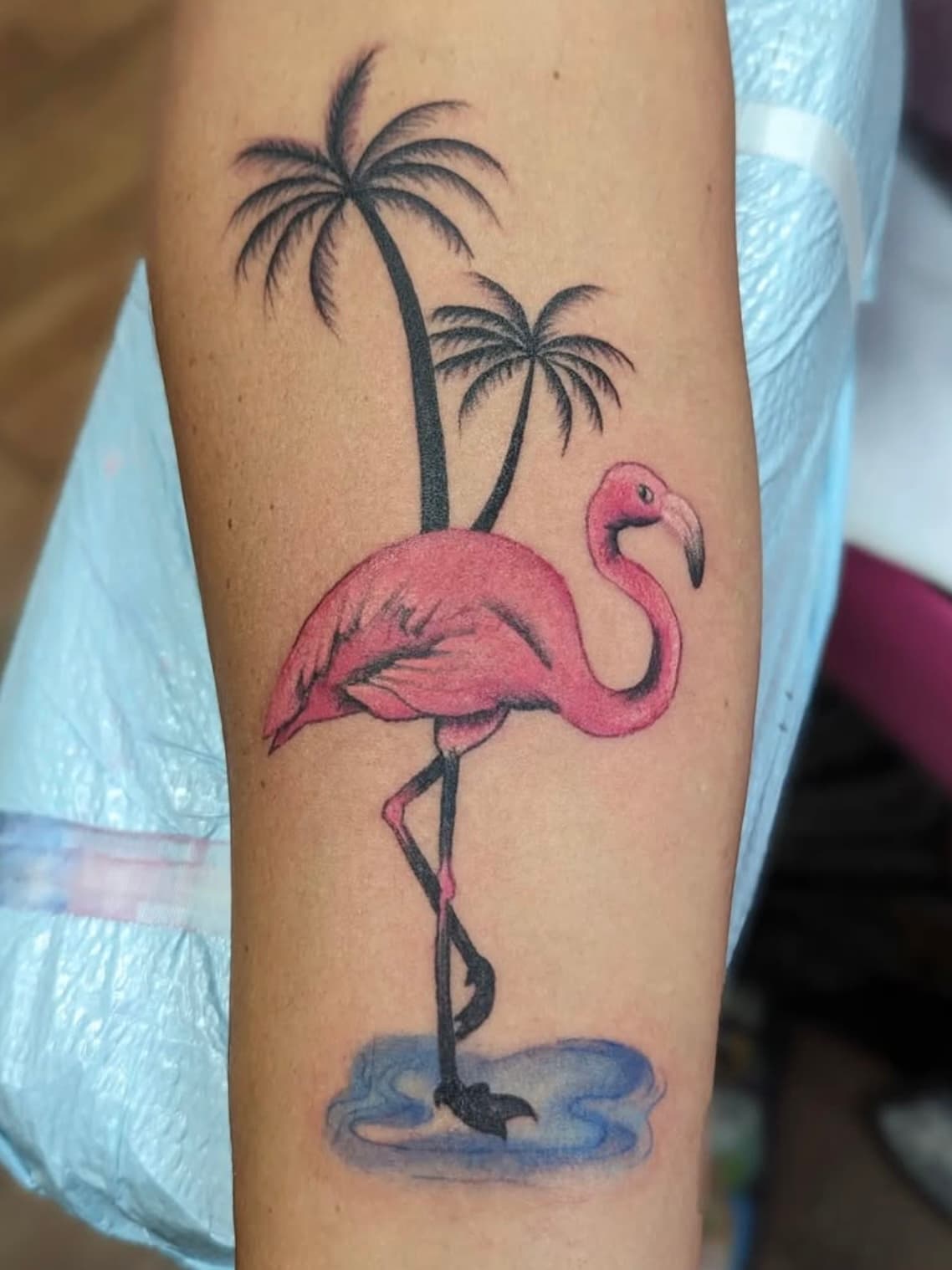 Pink flamingo tattoo with palm trees and blue water shadow detail