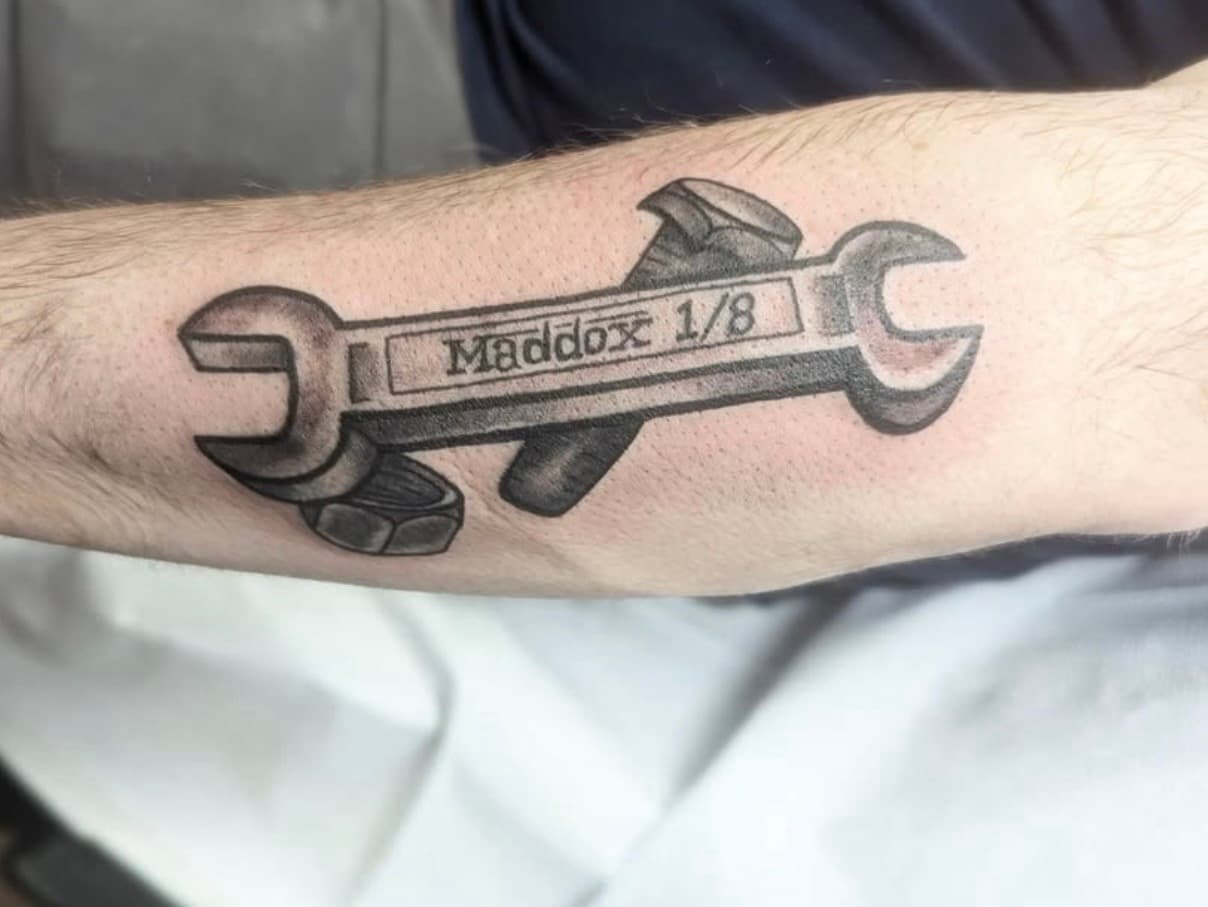 Black and grey tattoo of crossed Maddox wrenches on forearm